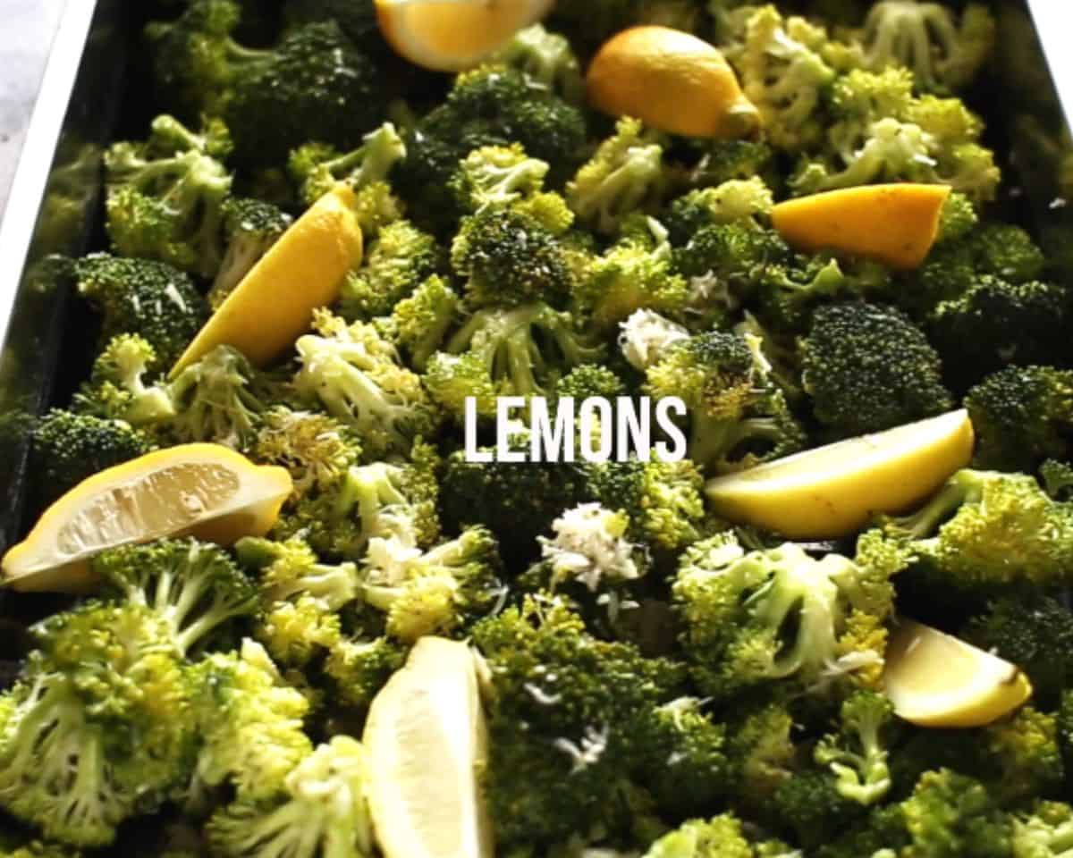Broccoli florets spread on a baking sheet with lemon wedges and Parmesan before going into the oven.