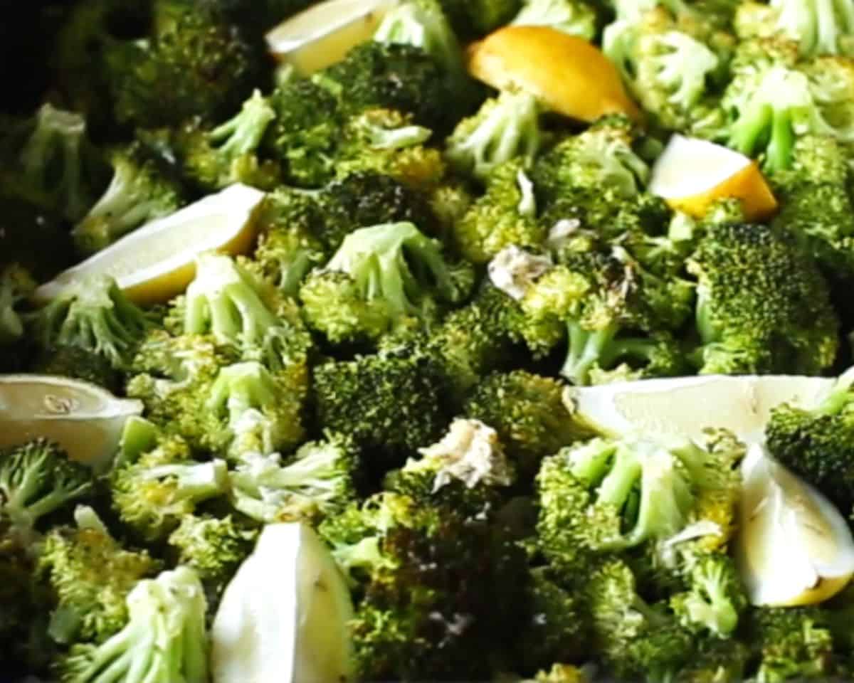 Close up of seasoned broccoli and lemon wedges arranged in a single layer on a sheet pan for roasting.