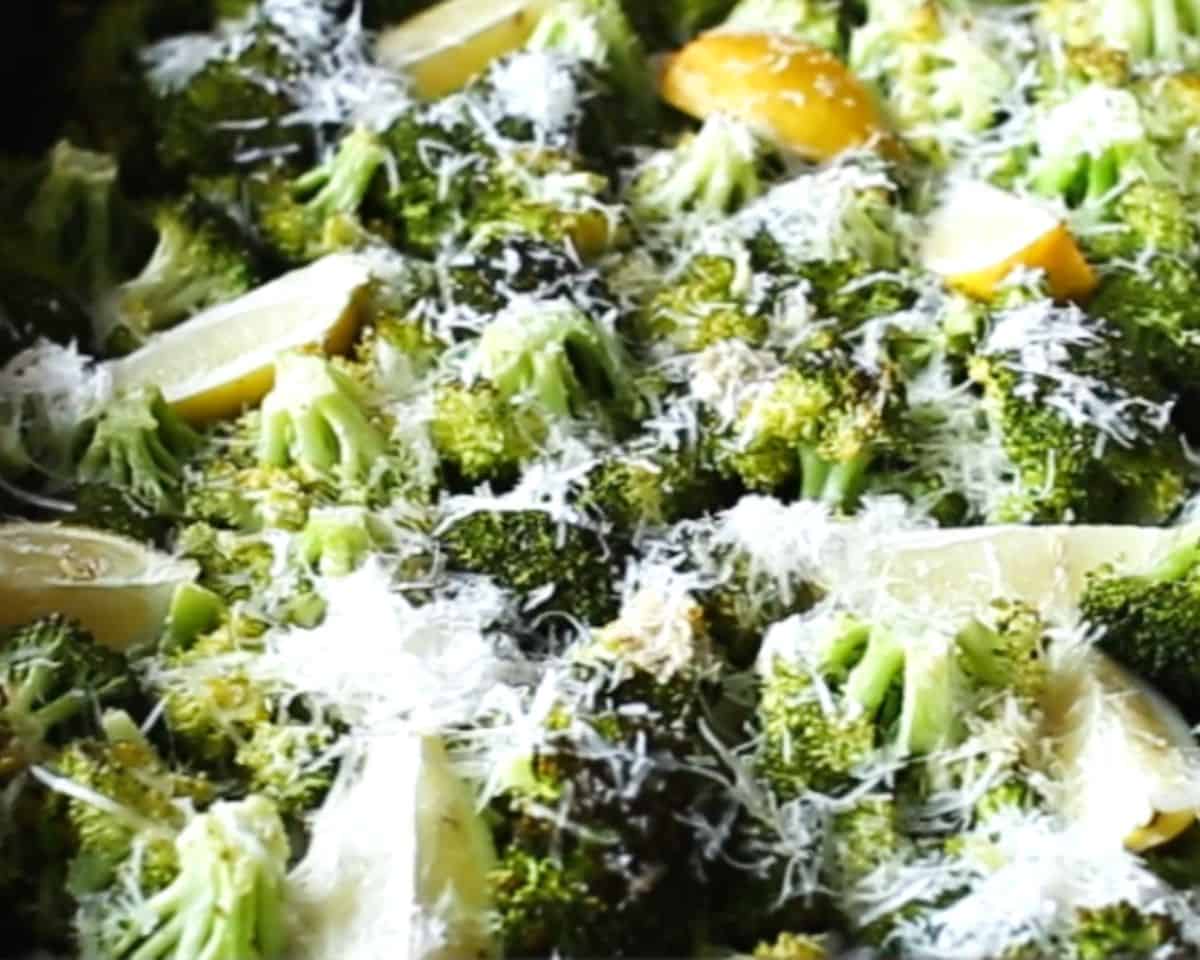 Roasted broccoli on a sheet pan sprinkled with freshly grated Parmesan cheese and lemon wedges.
