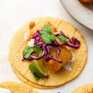 Crispy beer battered fish taco on a corn tortilla topped with shredded red cabbage, fresh cilantro, and a lime wedge.