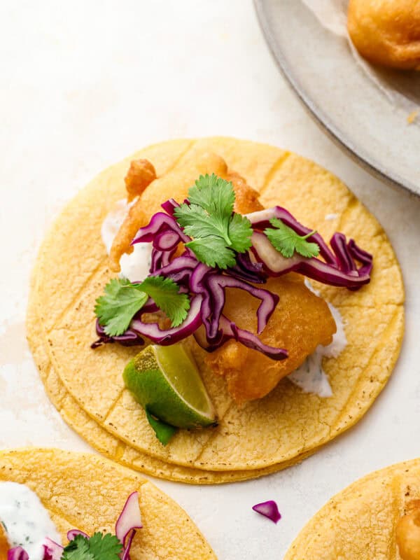 Crispy beer battered fish taco on a corn tortilla topped with shredded red cabbage, fresh cilantro, and a lime wedge.