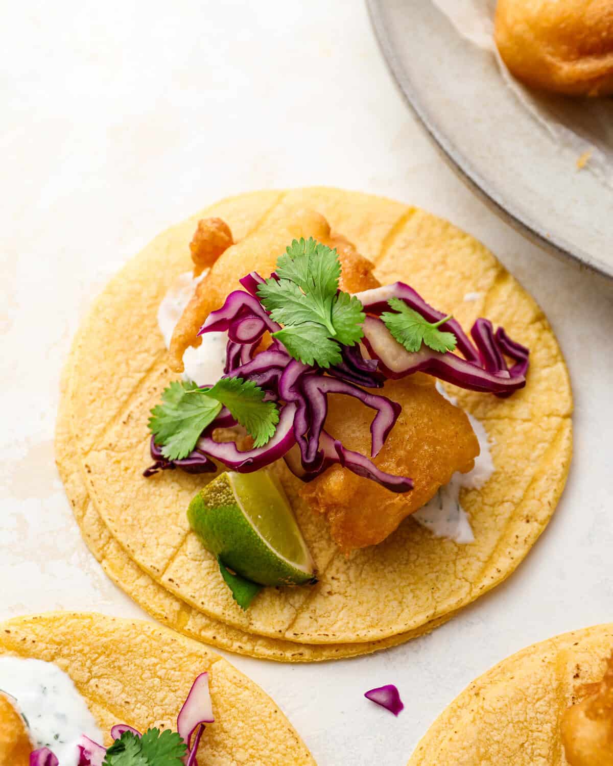 Crispy beer battered fish taco on a corn tortilla topped with shredded red cabbage, fresh cilantro, and a lime wedge.