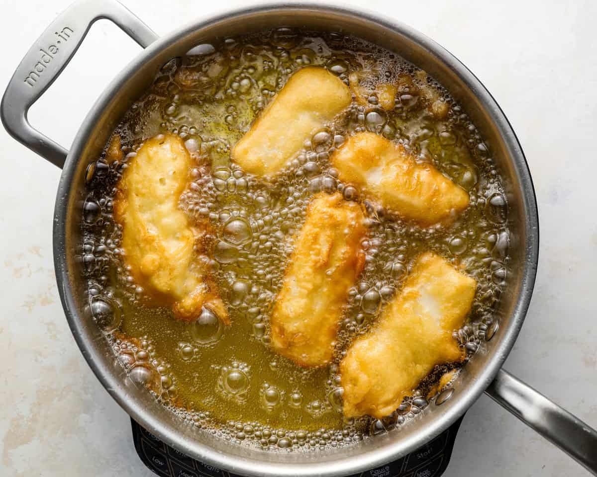 Beer battered fish frying in hot oil until golden and crispy.