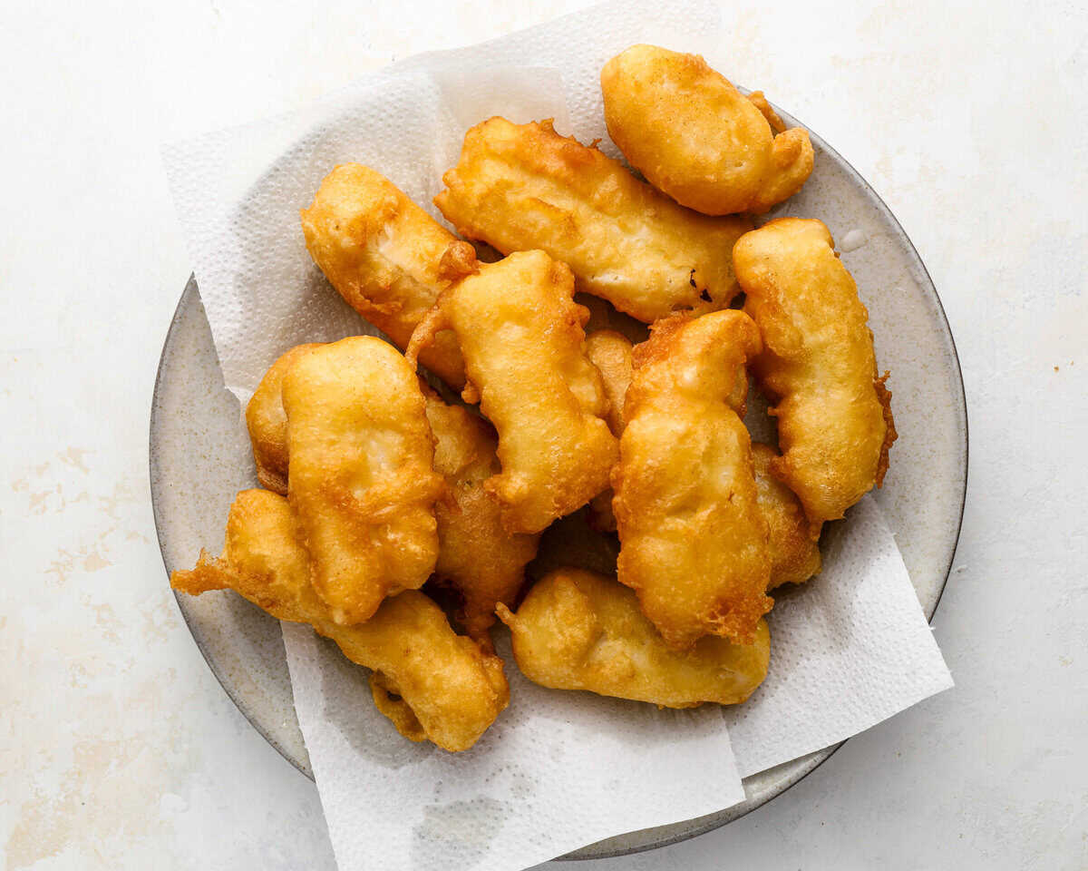 Golden beer battered fish draining on a paper towel-lined plate after frying.