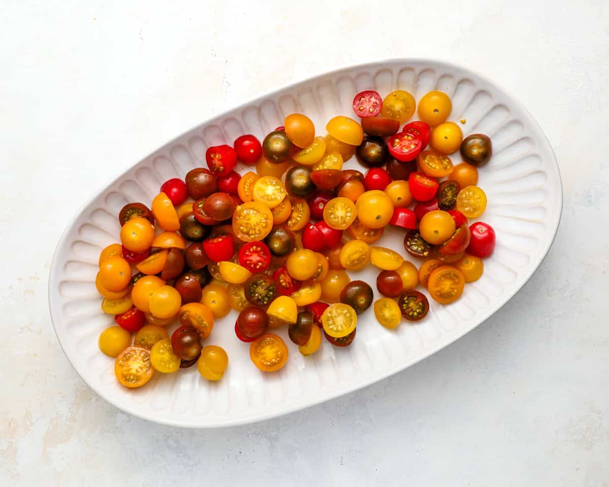 Halved cherry and grape tomatoes arranged on an oval serving dish before assembling the burrata caprese salad.