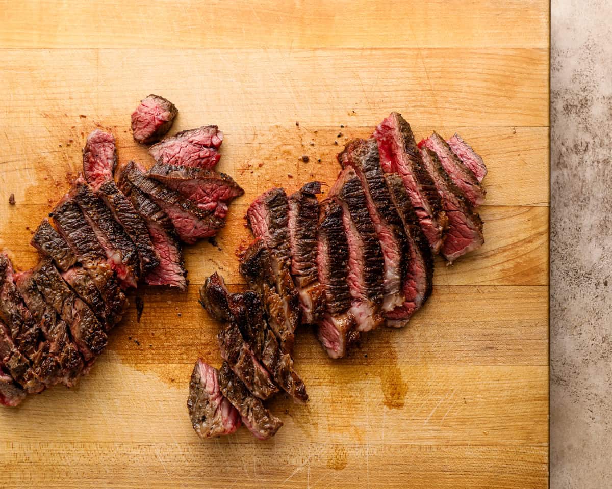 Denver steak sliced against the grain on a cutting board showing a juicy pink center