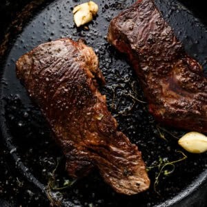Cooked Denver steaks searing in a cast iron skillet with garlic and thyme, showing a deep brown crust