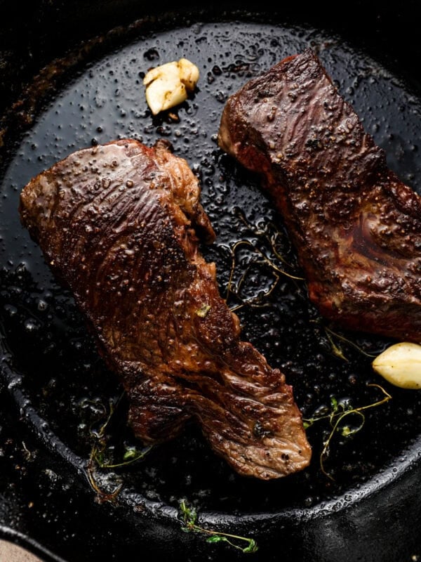 Cooked Denver steaks searing in a cast iron skillet with garlic and thyme, showing a deep brown crust