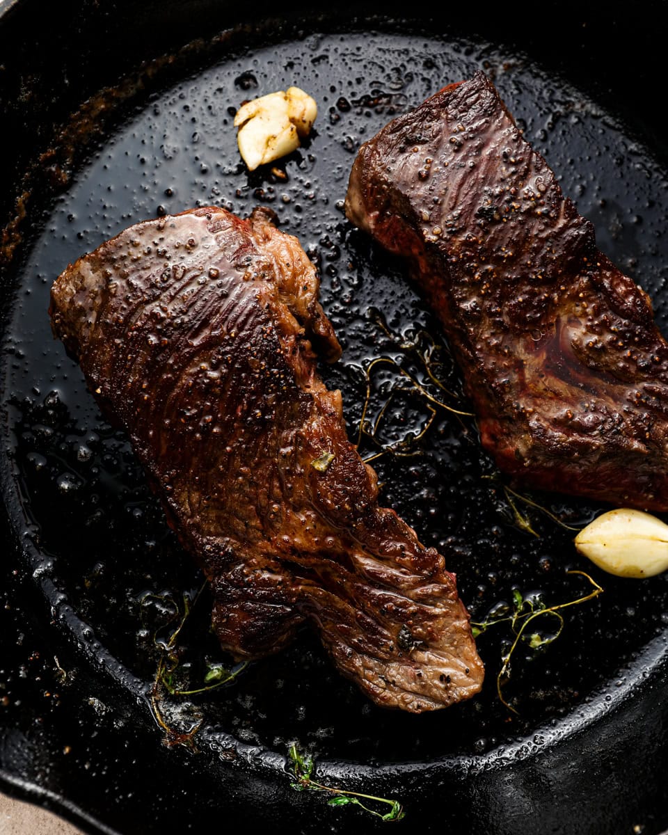Cooked Denver steaks searing in a cast iron skillet with garlic and thyme, showing a deep brown crust