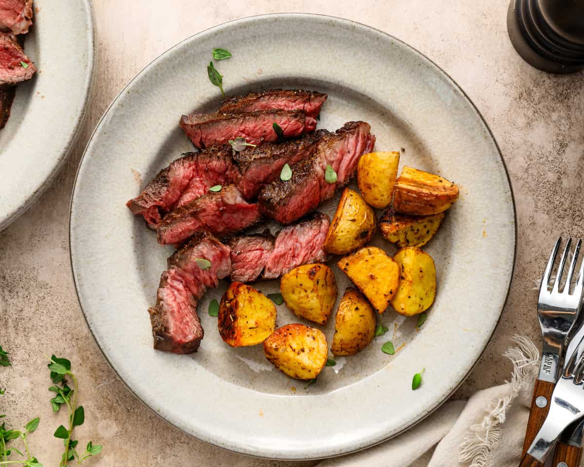 Sliced Denver steak served with roasted potatoes on a plate for a complete steak dinner