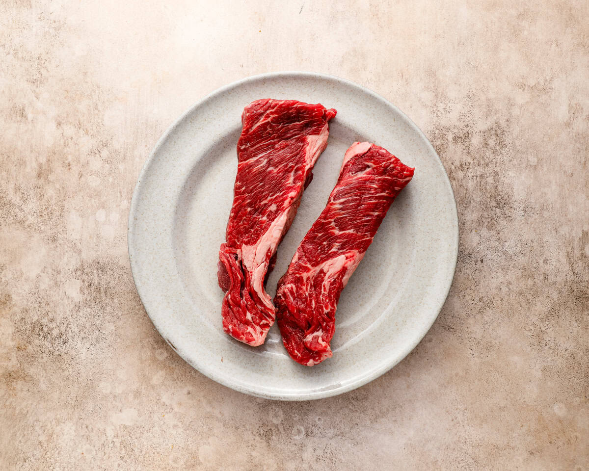 Raw Denver steaks on a white plate showing heavy marbling and thick cut from the chuck