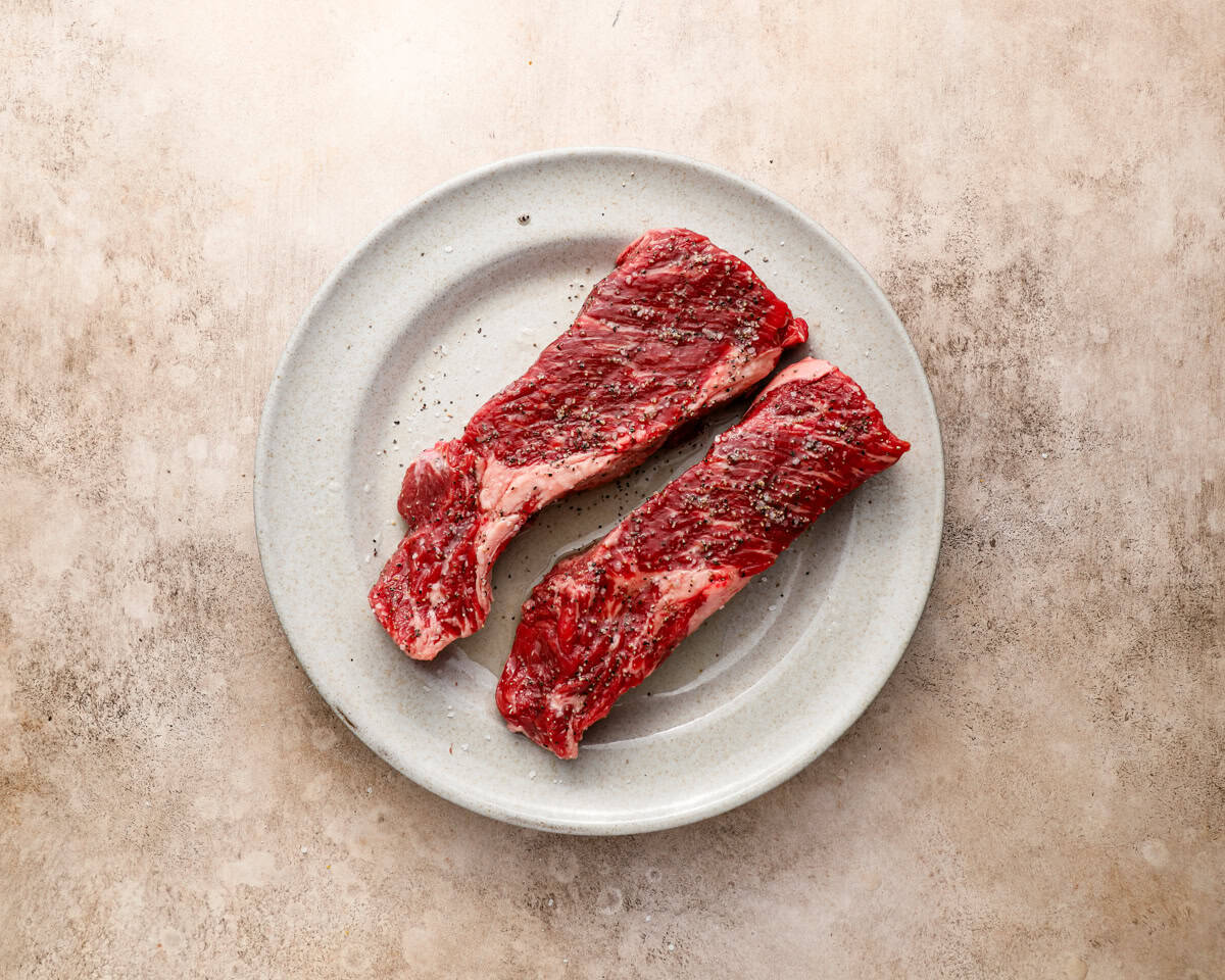Seasoned Denver steaks resting on a plate, ready to be seared in a hot pan