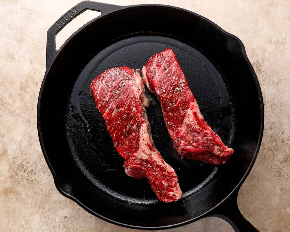 Seasoned Denver steaks placed into a hot cast iron skillet with oil to begin searing