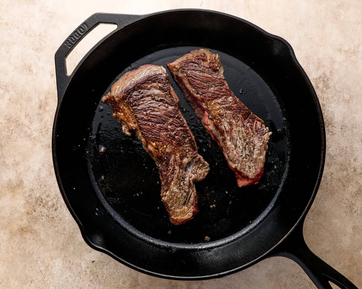 Denver steaks forming a brown crust while searing in a cast iron pan