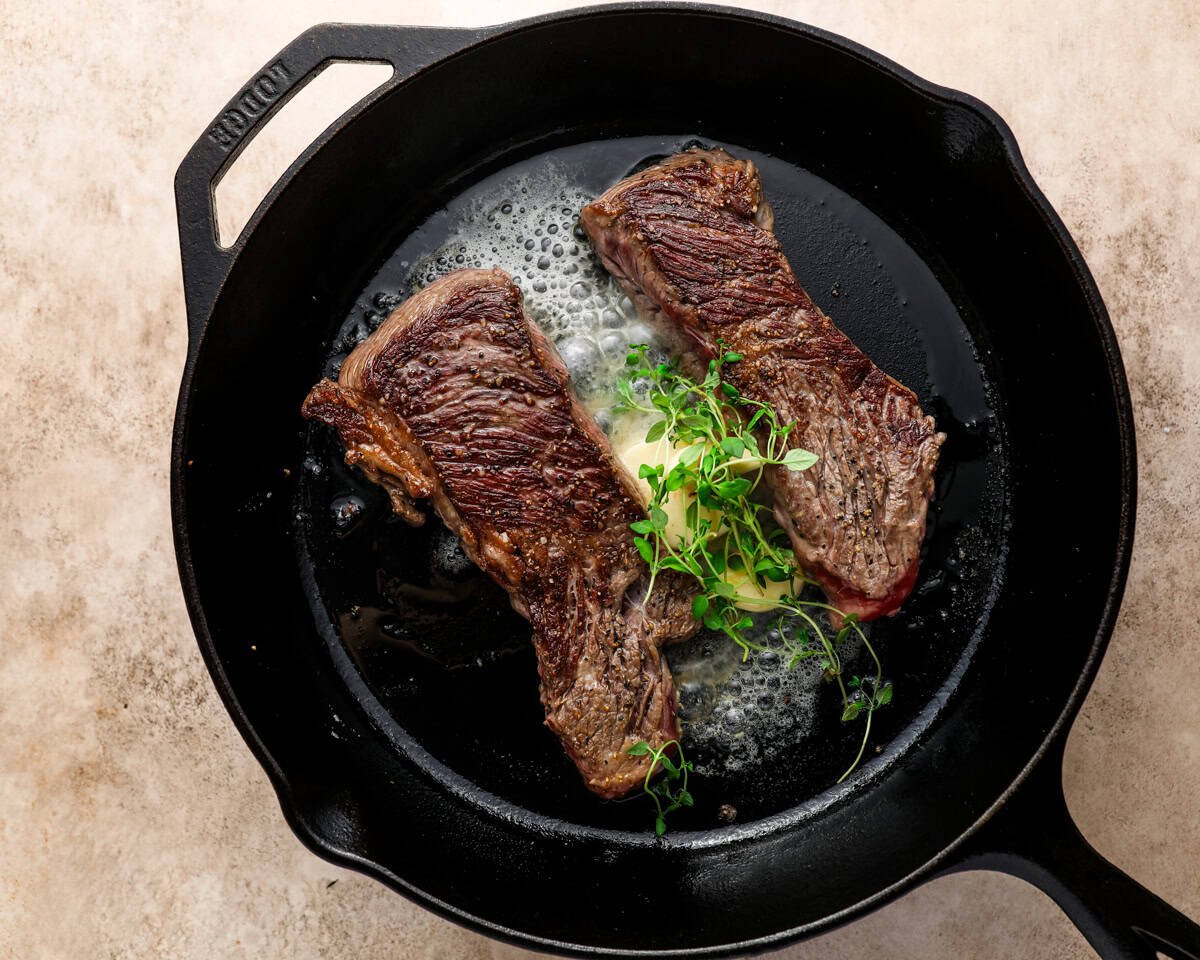 Denver steaks being basted with butter, garlic, and fresh thyme in a cast iron skillet