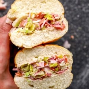 Chopped Italian sandwich cut in half, showing layers of chopped deli meats, provolone, lettuce, peppers, and dressing inside a soft hoagie roll.