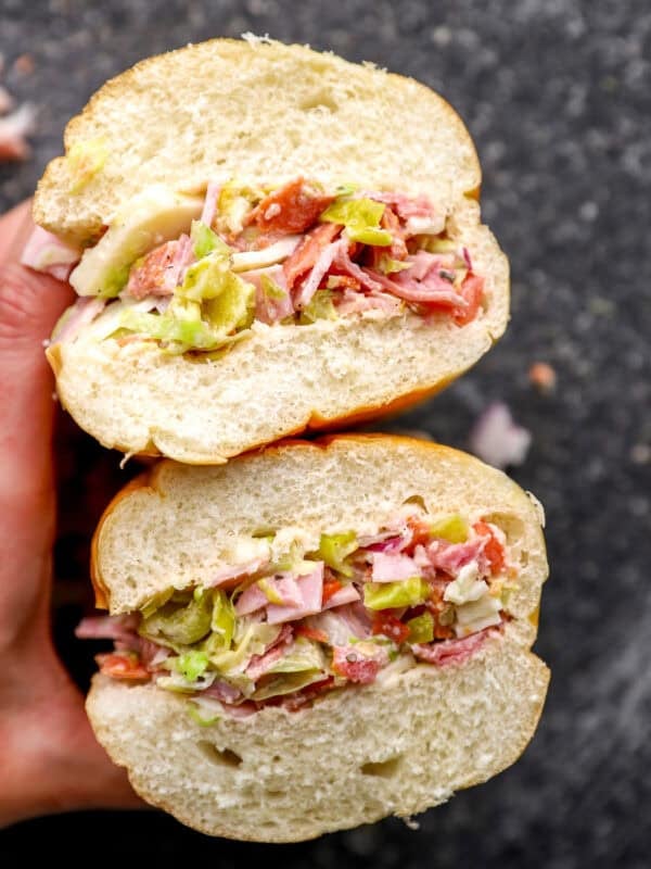 Chopped Italian sandwich cut in half, showing layers of chopped deli meats, provolone, lettuce, peppers, and dressing inside a soft hoagie roll.