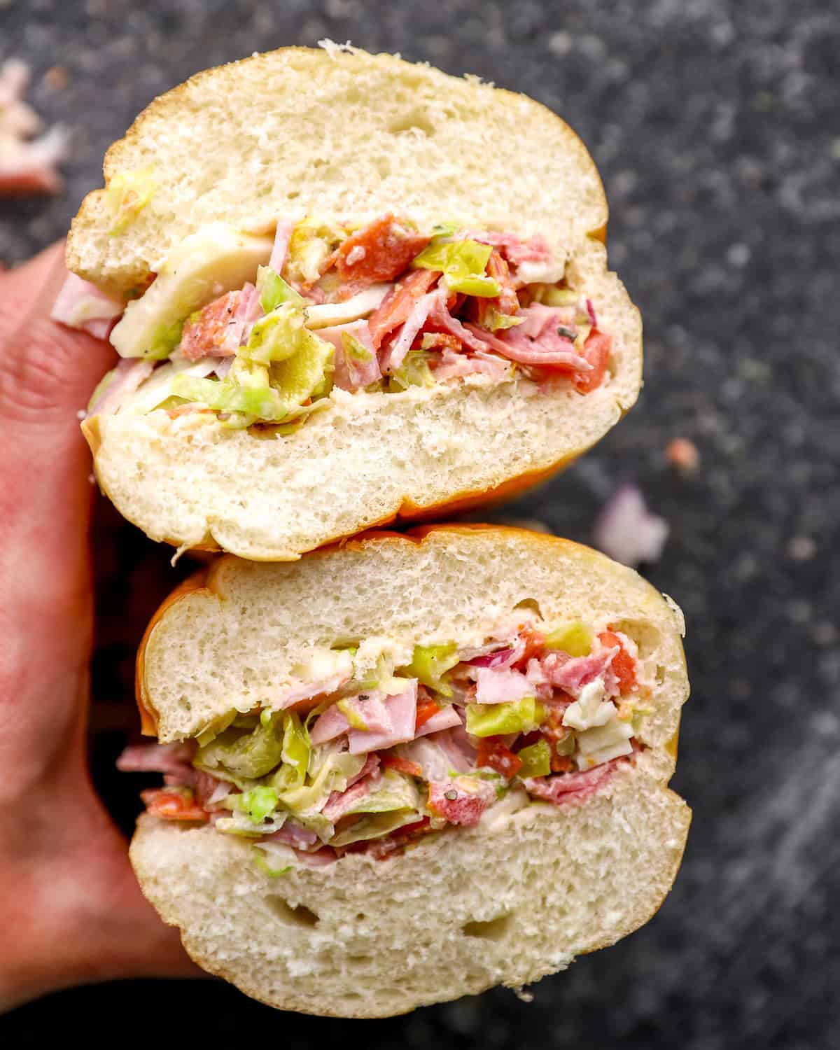 Chopped Italian sandwich cut in half, showing layers of chopped deli meats, provolone, lettuce, peppers, and dressing inside a soft hoagie roll.