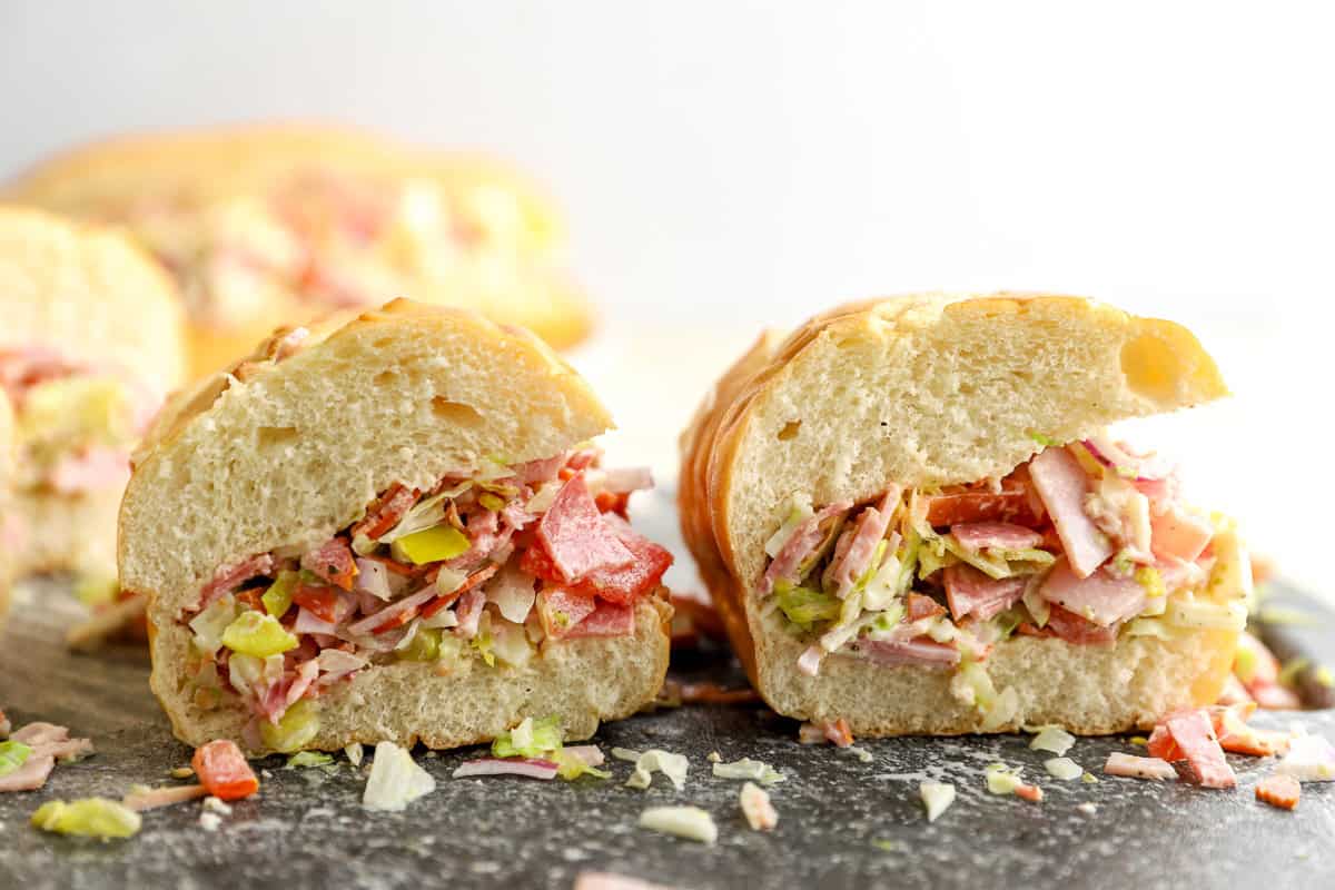 Two chopped Italian sandwiches cut in half, showing the chopped meat, cheese, vegetables, and dressing inside the rolls.