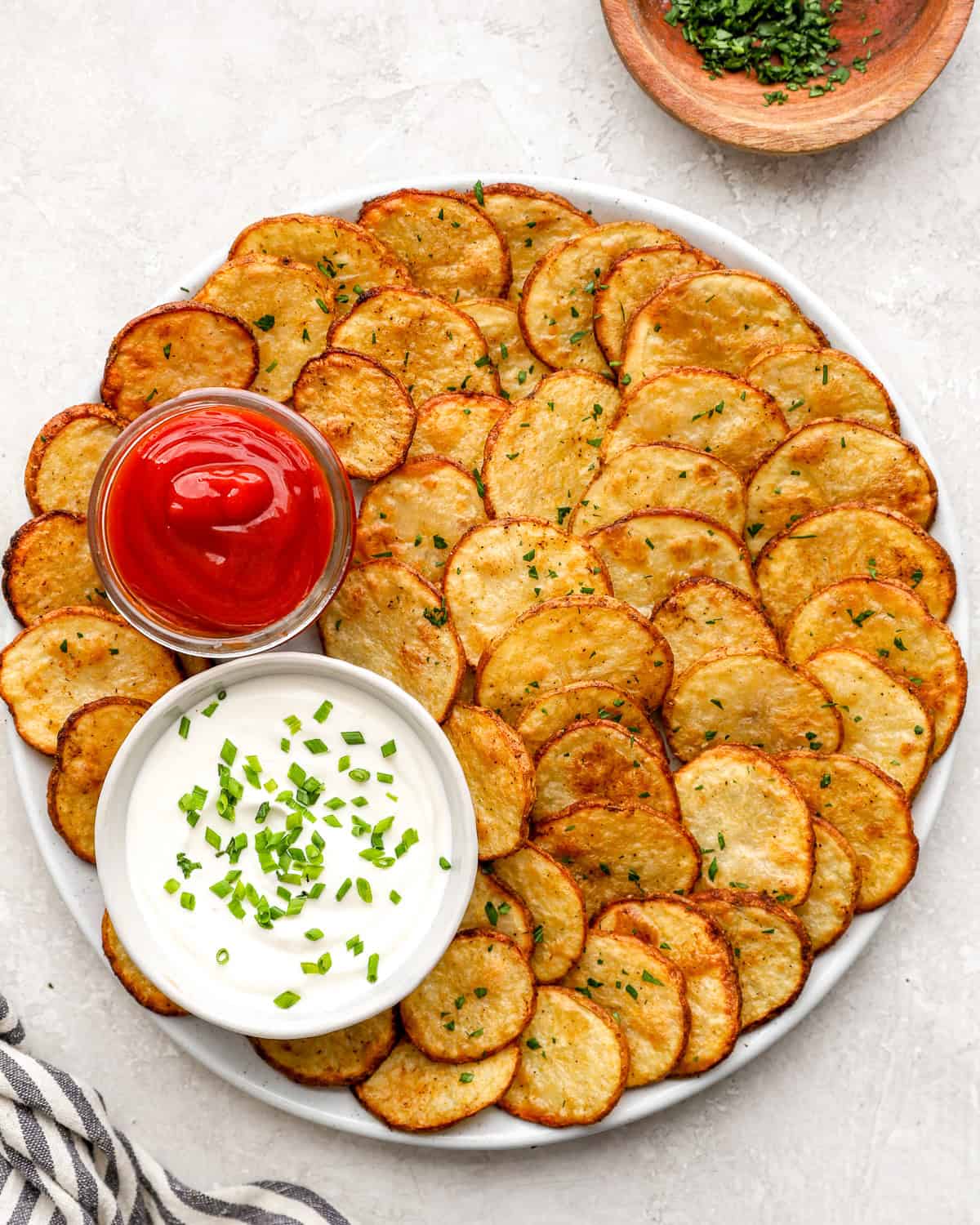 Crispy oven baked cottage fries arranged on a platter with ketchup and creamy dipping sauce, garnished with chopped herbs.