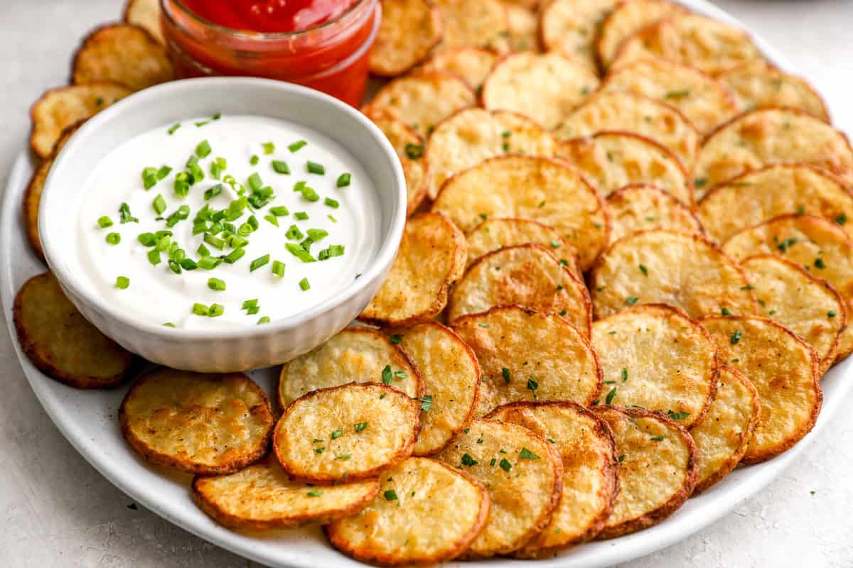 Crispy oven baked cottage fries arranged on a platter with creamy dipping sauce topped with chives and a jar of ketchup.