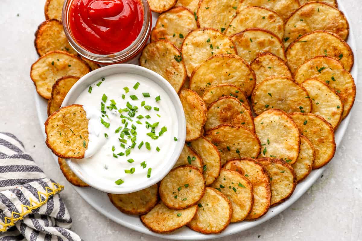 Golden cottage fries served with creamy dip and ketchup, with one potato slice dipped into the sauce.