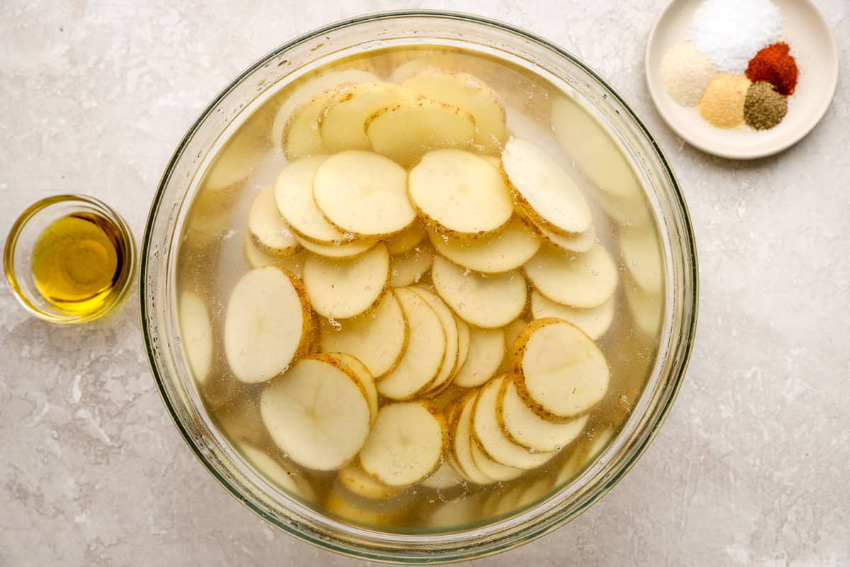 Sliced russet potatoes soaking in a bowl of water to remove excess starch before baking.