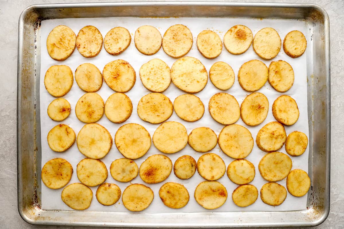 Seasoned potato rounds arranged in a single layer on a parchment-lined baking sheet.