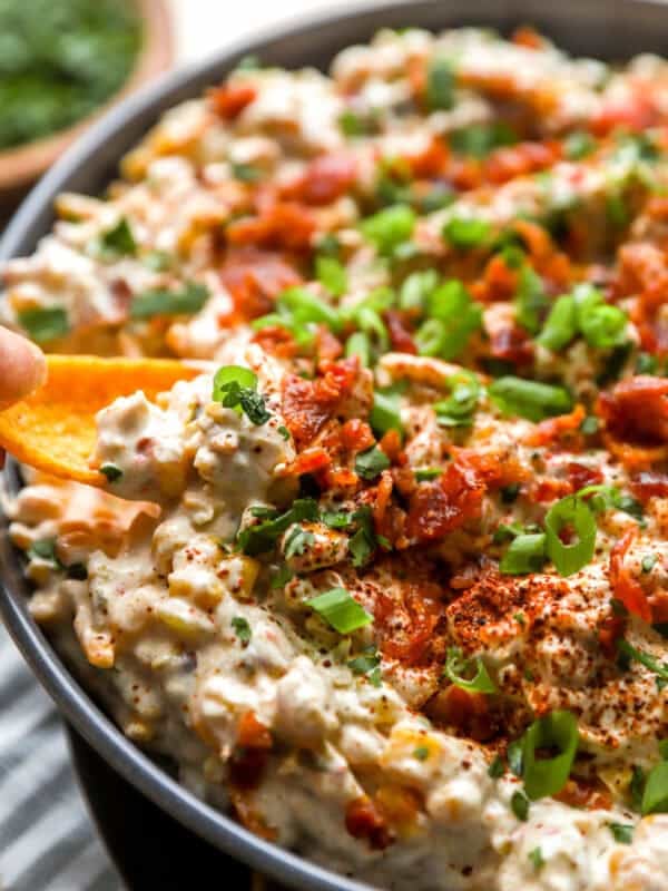 Crack corn dip topped with bacon, green onions, and seasoning, served in a bowl with a Fritos Scoop dipping in.