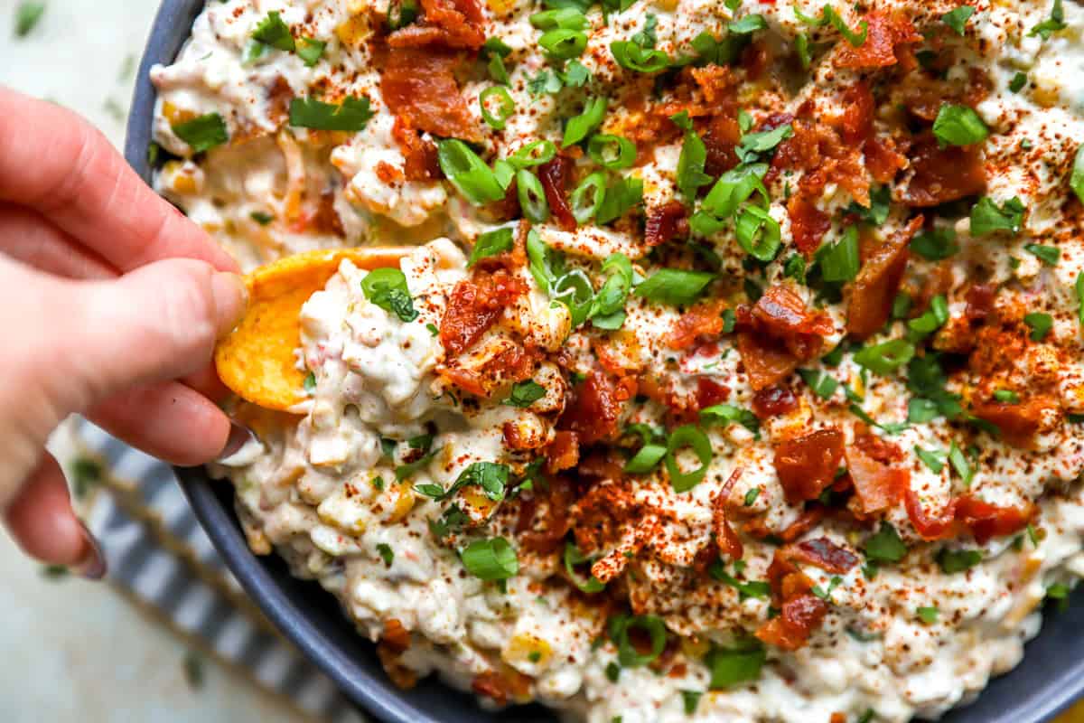 Creamy crack corn dip garnished with bacon and green onions, served with Fritos Scoops for dipping.