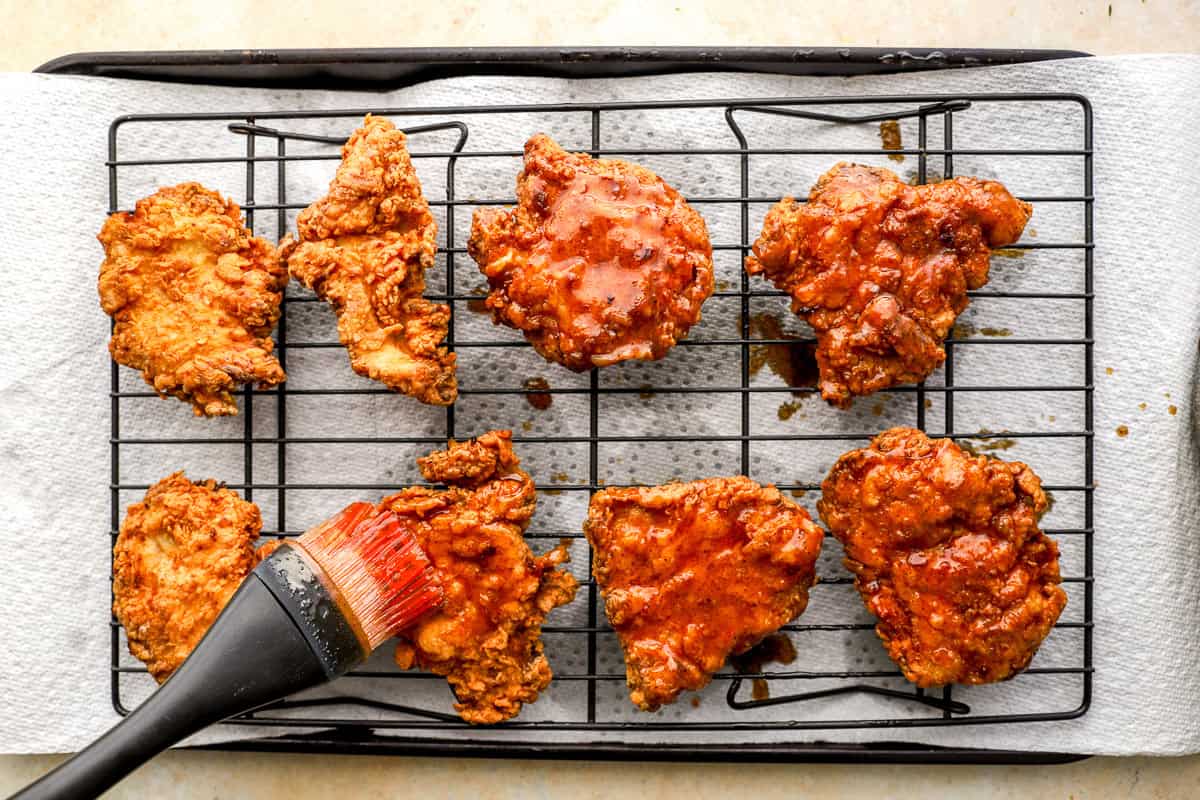 Hot honey sauce being brushed over crispy fried chicken pieces on a wire rack.