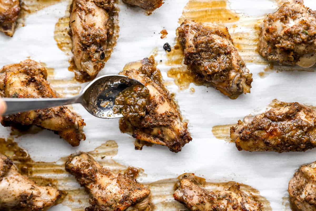 Brushing jerk marinade onto chicken wings halfway through baking on a parchment lined sheet pan