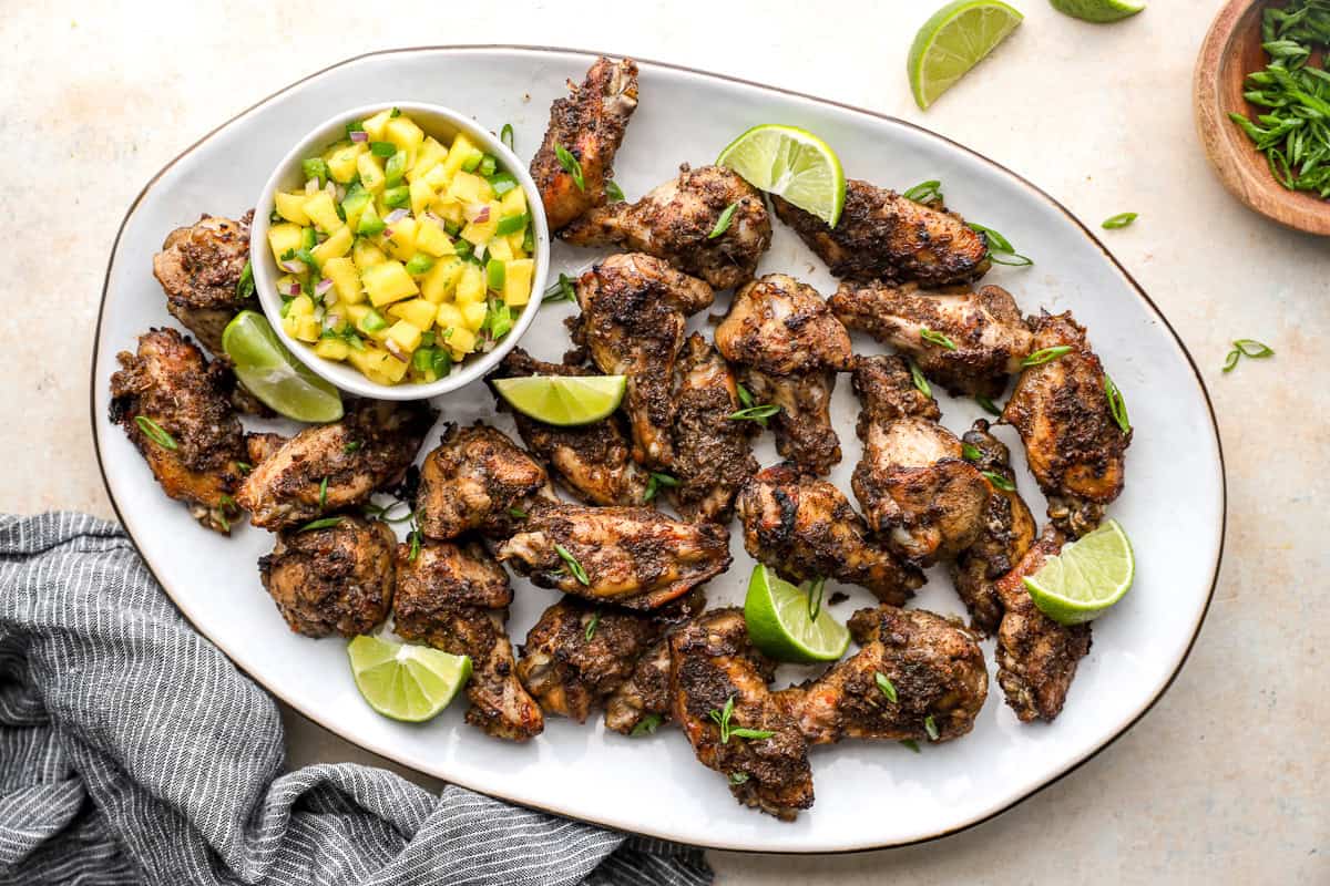 Oven baked jerk chicken wings arranged on a platter with pineapple salsa and fresh lime