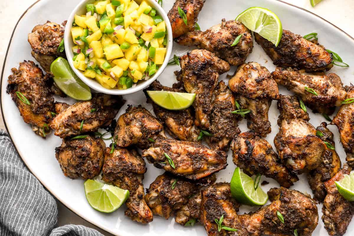 Close up of crispy jerk chicken wings with chopped green onion and lime wedges