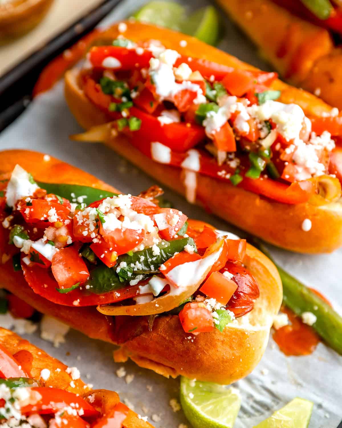 Bacon-wrapped Mexican hot dogs topped with peppers, jalapeños, pico de gallo, cotija cheese, and sour cream in toasted buns.