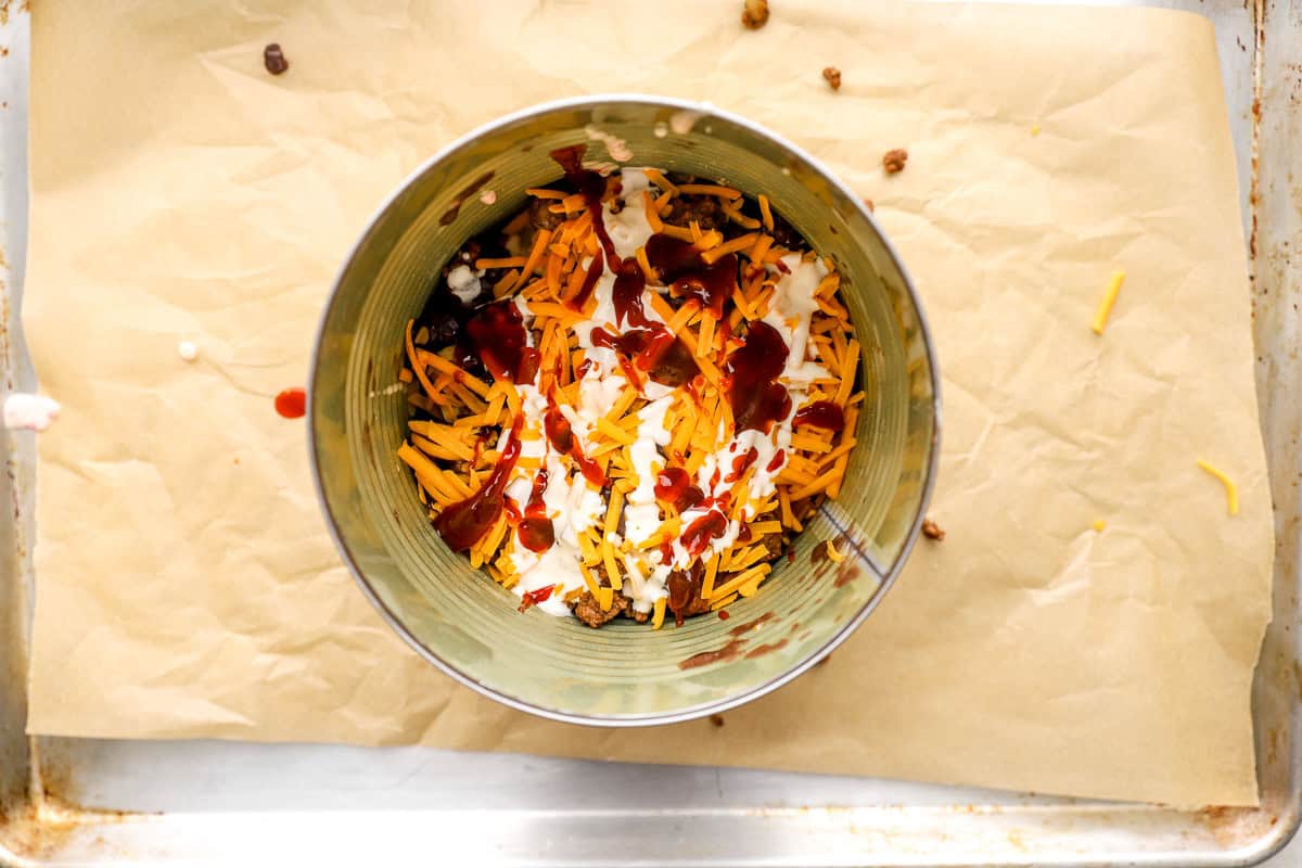 Tortilla chips, shredded cheese, sour cream, and BBQ sauce layered inside a large can for trash can nachos
