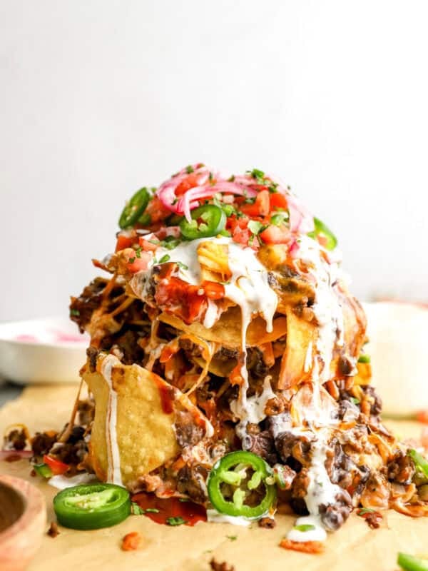 Tall trash can nachos stacked with tortilla chips, seasoned beef, black beans, melted cheese, sour cream, jalapeños, pico de gallo, and pickled onions