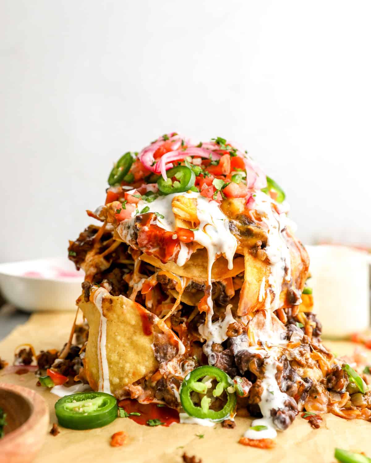 Tall trash can nachos stacked with tortilla chips, seasoned beef, black beans, melted cheese, sour cream, jalape&ntilde;os, pico de gallo, and pickled onions