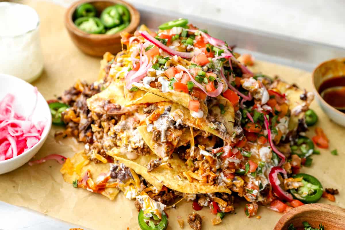 Trash can nachos served on a sheet pan with melted cheese, seasoned beef, black beans, jalapeños, pico de gallo, and pickled onions