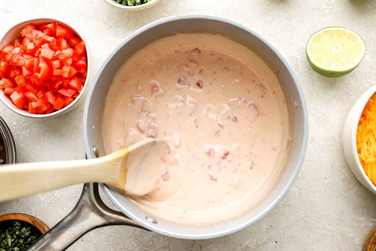 Smooth queso blanco cheese sauce with diced tomatoes and green chilies stirred in a saucepan