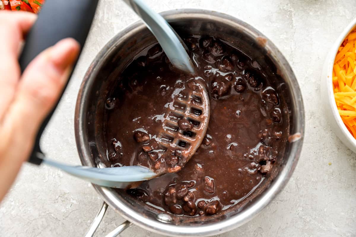 Black beans being lightly mashed in a saucepan to create a thick, scoopable texture for nachos