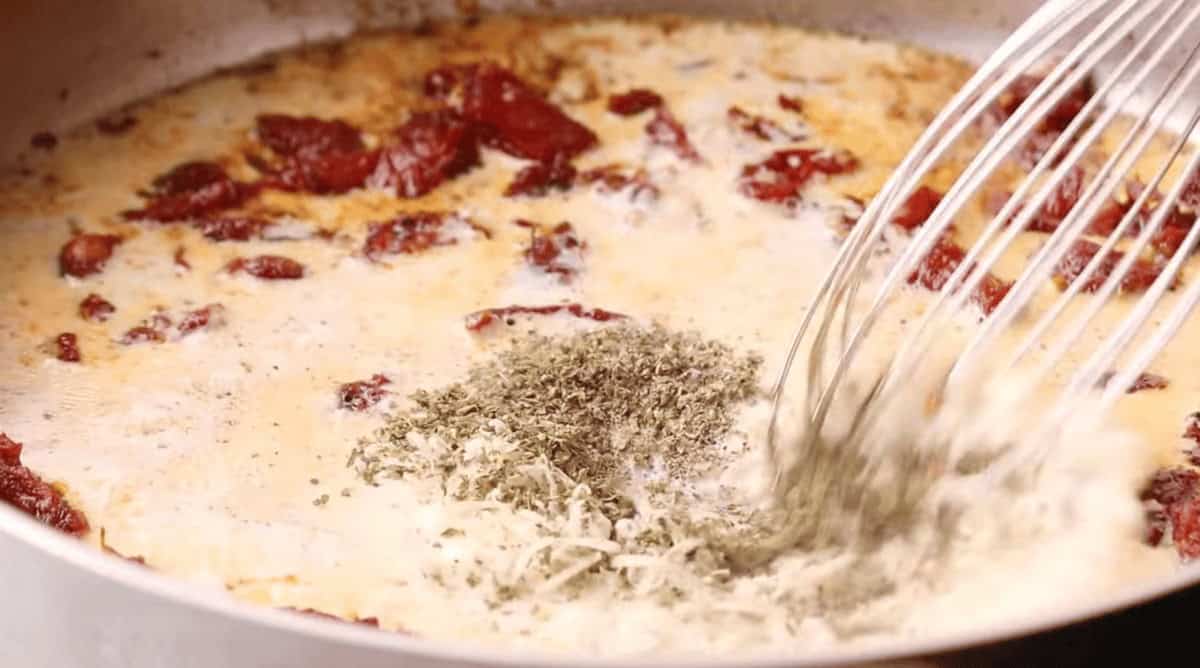 Tuscan chicken being cooked in a pan full of dried tomatoes soaked in oil.