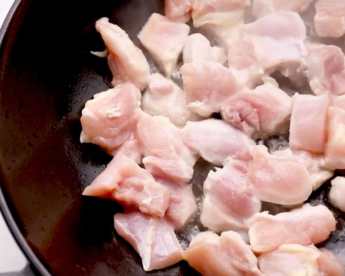 Bite-sized chicken thigh pieces cooking in a hot skillet, beginning to sear for chicken stir fry