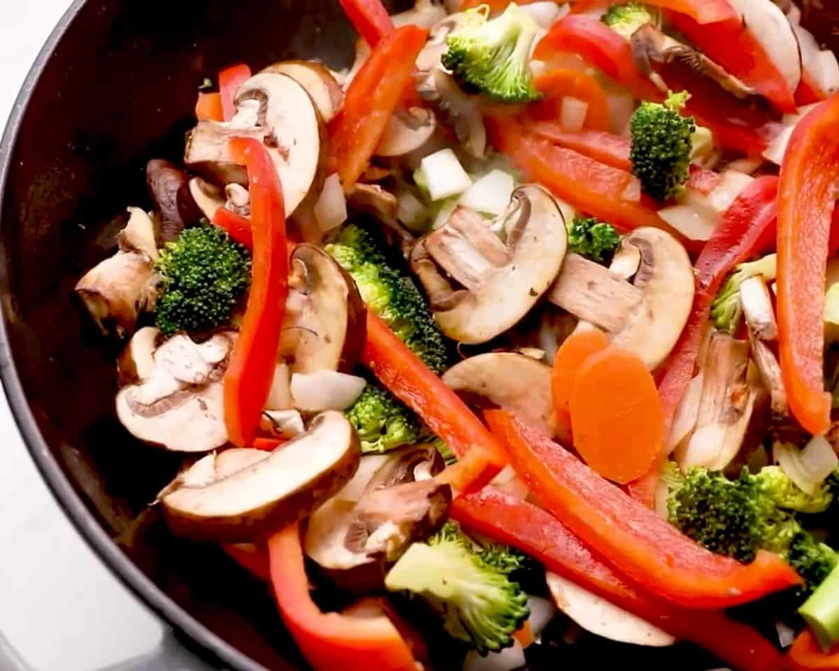 Fresh vegetables including broccoli, red bell pepper, mushrooms, carrots, and onion cooking in a skillet for stir fry