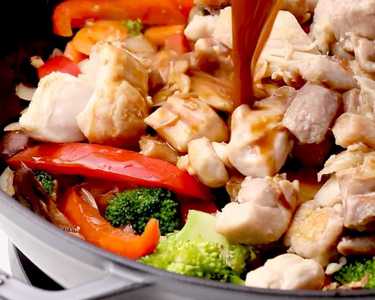 Homemade stir fry sauce being poured over chicken and vegetables in a skillet to create the glossy coating
