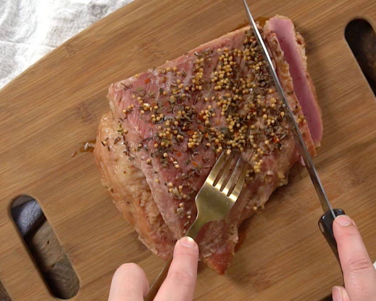 Cooked corned beef brisket resting on cutting board being sliced against the grain for tender texture