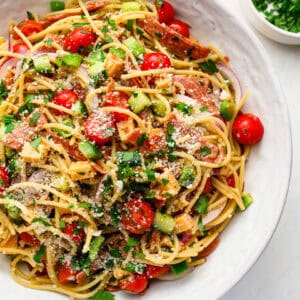 Spaghetti salad with Italian dressing, cheddar cubes, pepperoni, tomatoes, cucumber, red onion, parsley, and parmesan in a large bowl