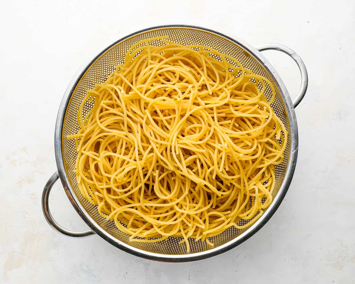 Cooked spaghetti draining in a colander after being rinsed with cold water