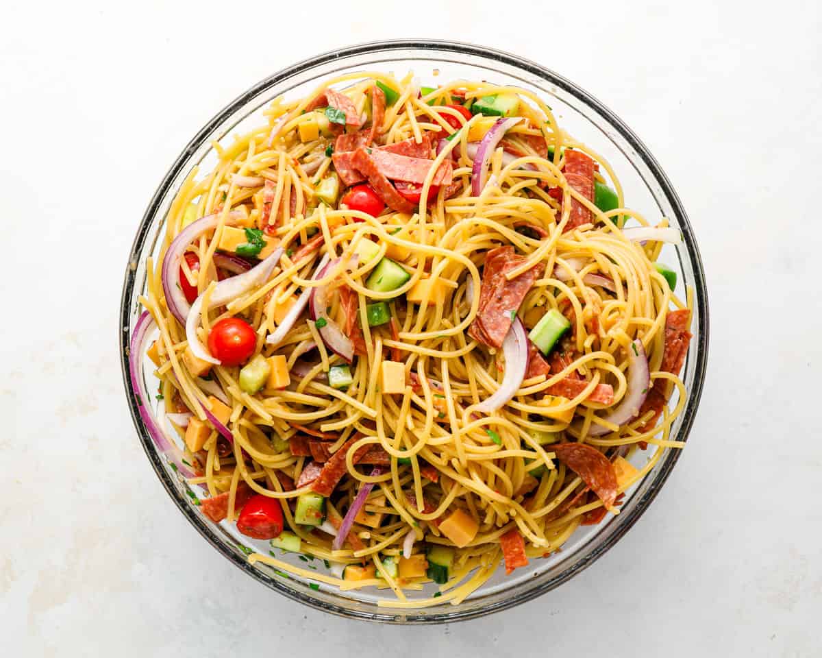Spaghetti salad tossed together with vegetables, cheese, and pepperoni in a mixing bowl