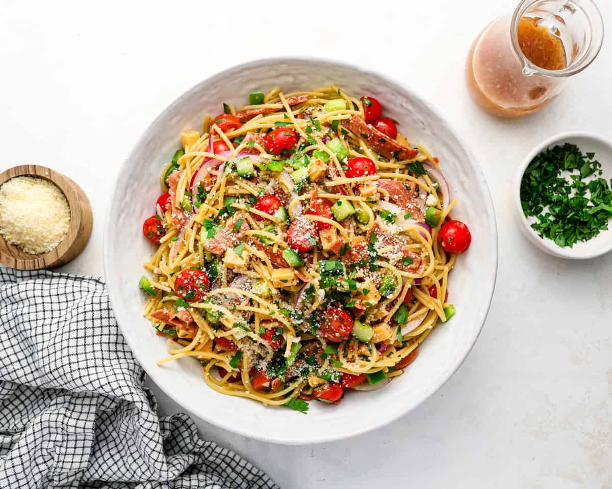 Finished spaghetti salad topped with parmesan and parsley with Italian dressing on the side